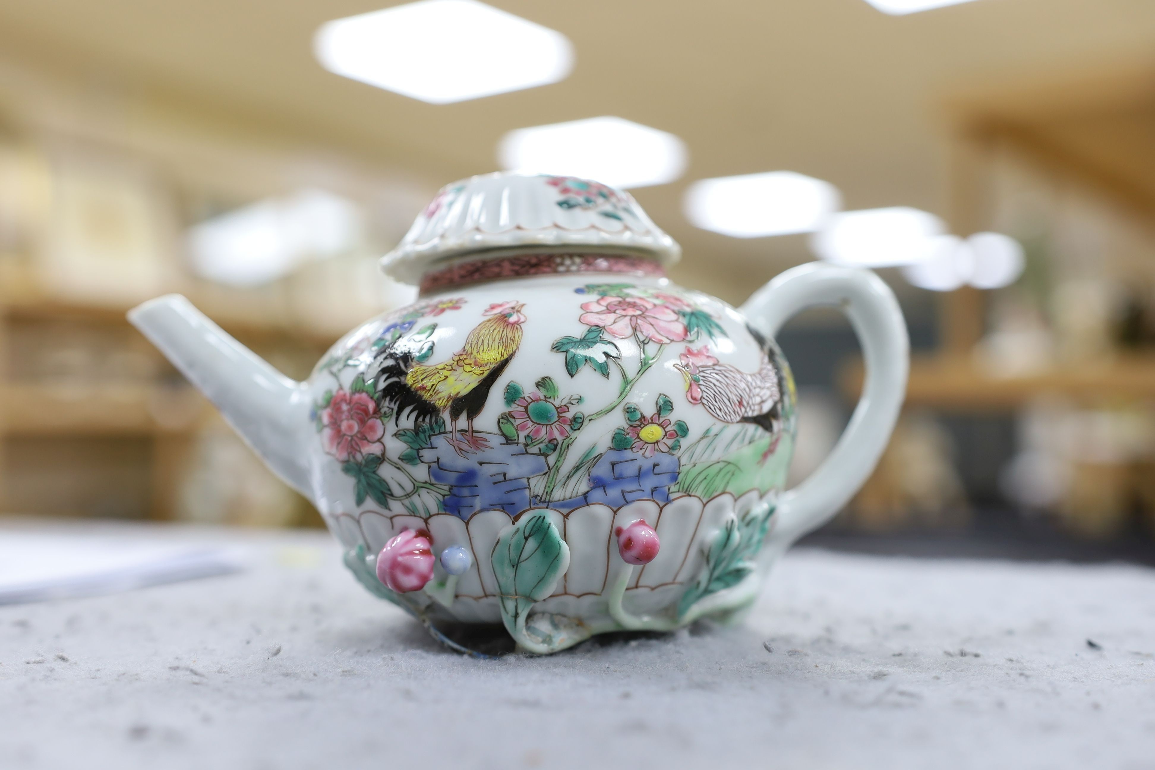 A Chinese famille rose chrysanthemum moulded teapot, early Qianlong period, painted with a cockerel amongst flowers, on a cage work base, 10 cms high
